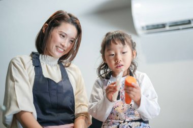 Japon bir ebeveyn ve çocuk, 30 'lu yaşlarda bir kadın, 20' li yaşlarda bir erkek ve 6 yaşında bir kız, evlerinin mutfağında havuç kesiyorlar..