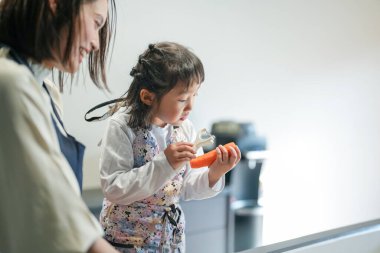 Japon bir ebeveyn ve çocuk, 30 'lu yaşlarda bir kadın, 20' li yaşlarda bir erkek ve 6 yaşında bir kız, evlerinin mutfağında havuç kesiyorlar..