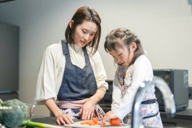 Japon bir ebeveyn ve çocuk, 30 'lu yaşlarda bir kadın, 20' li yaşlarda bir erkek ve 6 yaşında bir kız, evlerinin mutfağında havuç kesiyorlar..