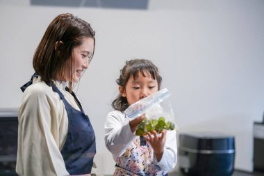 Japon bir ebeveyn ve çocuk, 30 'lu yaşlarda bir kadın, 20' li yaşlarda bir erkek ve 6 yaşında bir kız, evlerinin mutfağındaki bir çantaya salatalık koyarak Japon turşusu yapıyorlar..