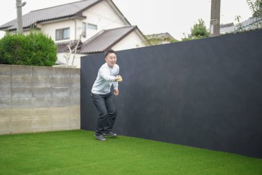 Japon bir ebeveyn ve çocuk, 20 'li yaşlarda bir adam ve 6 yaşında bir kız, evlerinin bahçesinde birbirlerine yeşil plastik toplar atarak oynuyorlar..