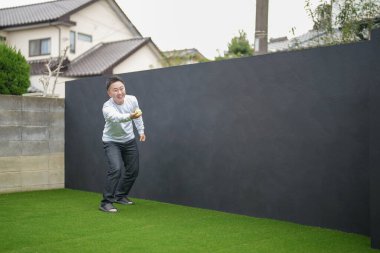 Japon bir ebeveyn ve çocuk, 20 'li yaşlarda bir adam ve 6 yaşında bir kız, evlerinin bahçesinde birbirlerine yeşil plastik toplar atarak oynuyorlar..