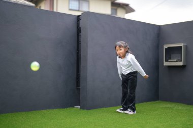 Japon bir ebeveyn ve çocuk, 20 'li yaşlarda bir adam ve 6 yaşında bir kız, evlerinin bahçesinde birbirlerine yeşil plastik toplar atarak oynuyorlar..