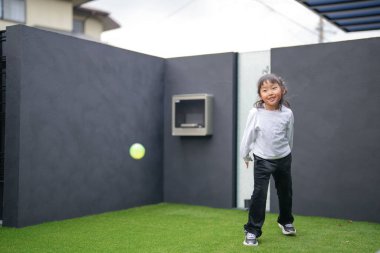 Japon bir ebeveyn ve çocuk, 20 'li yaşlarda bir adam ve 6 yaşında bir kız, evlerinin bahçesinde birbirlerine yeşil plastik toplar atarak oynuyorlar..
