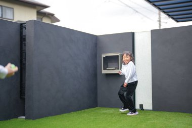 Japon bir ebeveyn ve çocuk, 20 'li yaşlarda bir adam ve 6 yaşında bir kız, evlerinin bahçesinde birbirlerine yeşil plastik toplar atarak oynuyorlar..