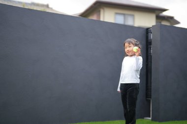 Japon bir ebeveyn ve çocuk, 20 'li yaşlarda bir adam ve 6 yaşında bir kız, evlerinin bahçesinde birbirlerine yeşil plastik toplar atarak oynuyorlar..