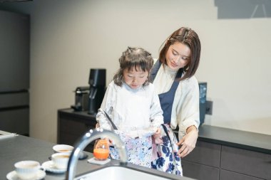 Japon bir ebeveyn ve çocuk, 30 'lu yaşlarda bir kadın, 20' li yaşlarda bir erkek ve 6 yaşındaki bir kız, evlerindeki mutfakta blender 'a doğranmış havuç ve bal ekleyerek meyve suyu içiyorlar..