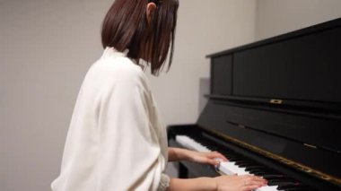 Genç Asyalı kadın oturma odasında piyano çalıyor..