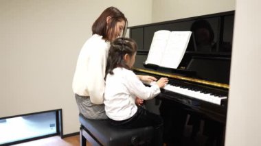 Genç bir kadın kızına piyano çalmayı öğretiyor.