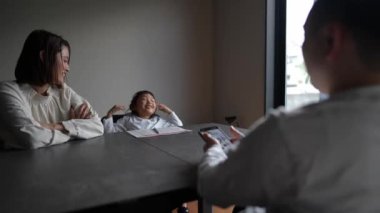 Anne ve kızı mutfakta ders veriyor, babası akıllı telefonlu.