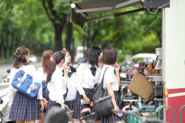 Haziran ayı başlarında, Pudong, Şangay 'da, yaz üniforması giymiş bir grup Japon liseli kız bir şehir caddesi boyunca okula gidiyor, yiyecek bir şeyler almak için bir gıda standına uğruyorlar..