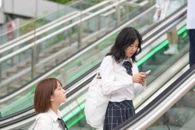 Yazın başlarında, Şangay 'da, Bund yakınlarında, üniformalı Japon liseli kızlar yürüyen merdivene biniyor, aynı üniformaları ve sessiz sohbetleri canlı şehir atmosferine gençlik enerjisi katıyor..