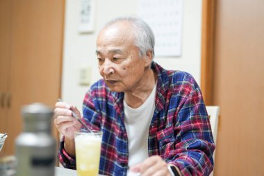 70 'li yaşlarının sonlarında kareli pijama giyen bir Japon, Japonya' da hafif aydınlatılmış bir apartman dairesinde tek başına viski içmekten hoşlanıyor. Sıcak atmosfer huzurlu bir bahar akşamının sessiz bir yansıması olduğunu gösteriyor..