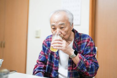 70 'li yaşlarının sonlarında kareli pijama giyen bir Japon, Japonya' da hafif aydınlatılmış bir apartman dairesinde tek başına viski içmekten hoşlanıyor. Sıcak atmosfer huzurlu bir bahar akşamının sessiz bir yansıması olduğunu gösteriyor..