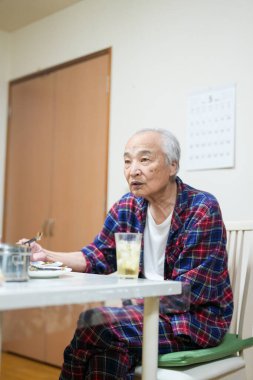 70 'li yaşlarının sonlarında kareli pijama giyen bir Japon, Japonya' da hafif aydınlatılmış bir apartman dairesinde tek başına viski içmekten hoşlanıyor. Sıcak atmosfer huzurlu bir bahar akşamının sessiz bir yansıması olduğunu gösteriyor..