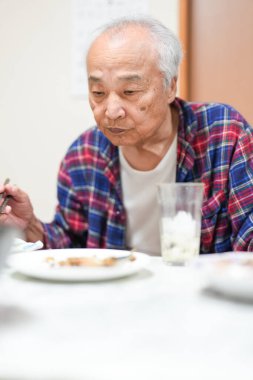 70 'li yaşlarının sonlarında kareli pijama giyen bir Japon, Japonya' da hafif aydınlatılmış bir apartman dairesinde tek başına viski içmekten hoşlanıyor. Sıcak atmosfer huzurlu bir bahar akşamının sessiz bir yansıması olduğunu gösteriyor..