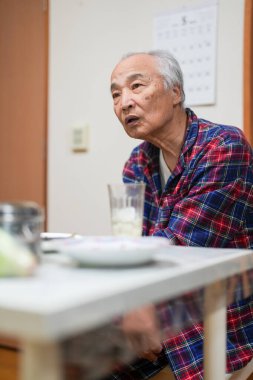 70 'li yaşlarının sonlarında kareli pijama giyen bir Japon, Japonya' da hafif aydınlatılmış bir apartman dairesinde tek başına viski içmekten hoşlanıyor. Sıcak atmosfer huzurlu bir bahar akşamının sessiz bir yansıması olduğunu gösteriyor..