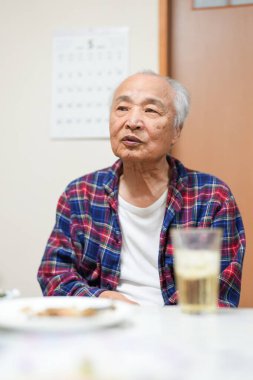 70 'li yaşlarının sonlarında kareli pijama giyen bir Japon, Japonya' da hafif aydınlatılmış bir apartman dairesinde tek başına viski içmekten hoşlanıyor. Sıcak atmosfer huzurlu bir bahar akşamının sessiz bir yansıması olduğunu gösteriyor..