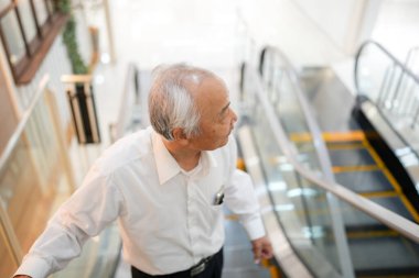 Japonya 'da kapalı bir yürüyen merdivende, 70' li yaşlarının sonlarında, temiz beyaz bir gömlek giyen bir Japon, sakin bir tavırla yürüyen merdivene biniyor,.