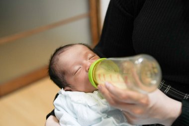 İki haftalık bir Japon bebeği geleneksel bir tatami odasında yatar, annesi tarafından bir şişeden sütle huzur içinde beslenir, yazın erken zamanlarının yumuşak sıcaklığı ve yumuşak atmosferiyle çevrelenir..