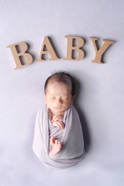 İki haftalık bir Japon bebeğinin lavanta arka planında yumuşak bir kundakta uyurken çekilmiş yeni doğan fotoğrafı. Tahta bloklar 'Bebek' in yakınına yerleştiriliyor, sahnenin cazibesini arttırıyor..