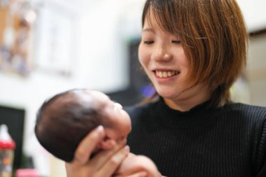 Yarım aylık bir Japon bebek pembe bir battaniyeye sarılır ve genç annesi tarafından yirmili yaşlarının başında, sakin ve huzurlu bir ifadeyle nazikçe omzuna bastırılarak geğirilir..