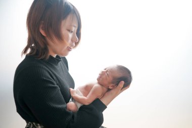 Beyaz arka planda yeni doğan bir bebeğin resmi. Bebek bezli iki haftalık bir bebek. Genç bir Japon anne tarafından 20 'li yaşlarının başında sevgiyle kucaklanıyor. Minimalist ve iç açıcı profesyonel fotoğrafçılık.