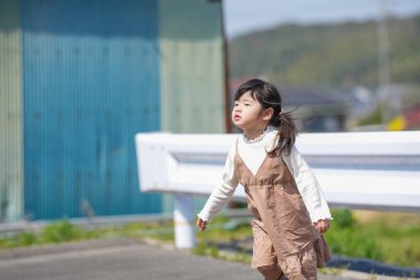 3 yaşında bir Japon kız beyaz bir korkuluğun yanında duruyor, sessizce kırlara bakıyor. Mart ayı başlarında yakalanan dişi, sakin bahar melteminin ve kırsal bir ortamda hafif güneş ışığının tadını çıkarıyor..