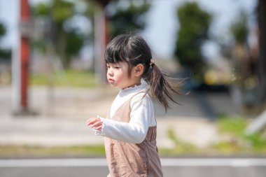 İkiz kuyruklu 3 yaşında Japon bir kız sakin bir kırsal yolda mutlu bir şekilde koşuyor. Mart başında yakalanan yumuşak bahar esintisi ve güneş ışığı onun neşeli ve kaygısız ruhunu vurguluyor..