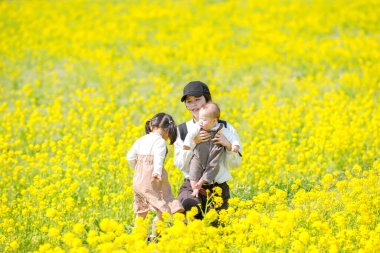30 'lu yaşlarda Japon bir anne, 6 aylık bebeğini kucağında 3 yaşındaki ikiz kuyruklu kızıyla kırsalda çiçek açan bir tarlada oturuyor. Mart ayı başlarında yakalandı..