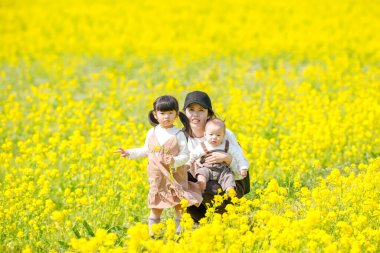 30 'lu yaşlarda Japon bir anne, 6 aylık bebeğini kucağında 3 yaşındaki ikiz kuyruklu kızıyla kırsalda çiçek açan bir tarlada oturuyor. Mart ayı başlarında yakalandı..