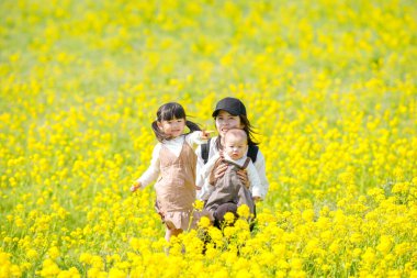 30 'lu yaşlarda Japon bir anne, 6 aylık bebeğini kucağında 3 yaşındaki ikiz kuyruklu kızıyla kırsalda çiçek açan bir tarlada oturuyor. Mart ayı başlarında yakalandı..