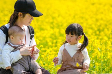 30 'lu yaşlarda Japon bir anne, kırsal bir tarlada çiçek açan bir bankta, 6 aylık bebeğini kucağında, 3 yaşındaki ikiz kuyruklu kızının yanında oturuyor. Mart ayı başlarında yakalandı..