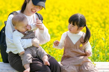 30 'lu yaşlarda Japon bir anne, kırsal bir tarlada çiçek açan bir bankta, 6 aylık bebeğini kucağında, 3 yaşındaki ikiz kuyruklu kızının yanında oturuyor. Mart ayı başlarında yakalandı..