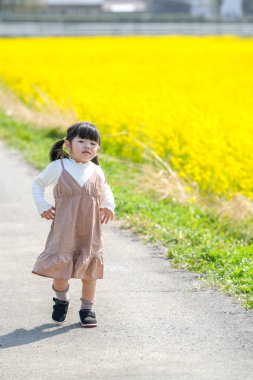 Huzurlu bir kırsal alanda, ikiz at kuyruklu 3 yaşındaki Japon bir kız Mart ayı başında çiçek açan kolza çiçeği tarlasında yürür ve baharın cazibesini somutlaştırır..