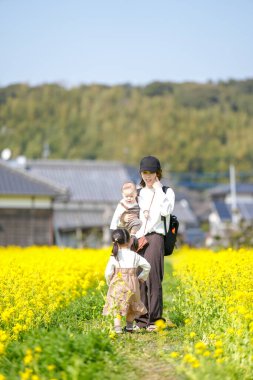 Mart ayı başlarında, Japon kırsalında, 6 aylık bir erkek bebek, ikiz kuyruklu 3 yaşında bir kız çocuğu, ve anneleri tamamen açan kolza çiçekleri arasında huzur içinde oturur, baharın tadını çıkarırlar..