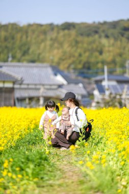 Mart ayı başlarında, Japon kırsalında, 6 aylık bir erkek bebek, ikiz kuyruklu 3 yaşında bir kız çocuğu, ve anneleri tamamen açan kolza çiçekleri arasında huzur içinde oturur, baharın tadını çıkarırlar..