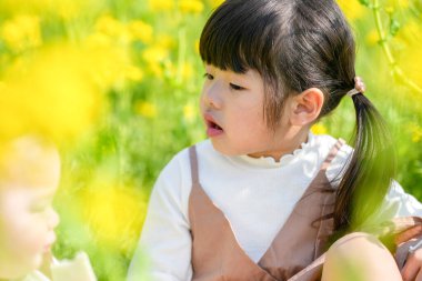 Mart ayında çiçek açan bir tecavüz tarlasında, 6 aylık Japon bir erkek bebek ve 3 yaşındaki ikiz kuyruklu bir kız birlikte oturur, altın çiçeklerle çevrili bahar güneşinin altında atıştırmalıkların tadını çıkarırlar..
