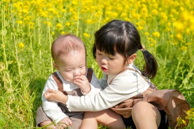 Mart ayında çiçek açan bir tecavüz tarlasında, 6 aylık Japon bir erkek bebek ve 3 yaşındaki ikiz kuyruklu bir kız birlikte oturur, altın çiçeklerle çevrili bahar güneşinin altında atıştırmalıkların tadını çıkarırlar..