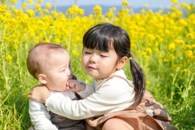 Mart ayında çiçek açan bir tecavüz tarlasında, 6 aylık Japon bir erkek bebek ve 3 yaşındaki ikiz kuyruklu bir kız birlikte oturur, altın çiçeklerle çevrili bahar güneşinin altında atıştırmalıkların tadını çıkarırlar..