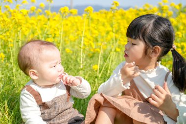 Mart ayında çiçek açan bir tecavüz tarlasında, 6 aylık Japon bir erkek bebek ve 3 yaşındaki ikiz kuyruklu bir kız birlikte oturur, altın çiçeklerle çevrili bahar güneşinin altında atıştırmalıkların tadını çıkarırlar..