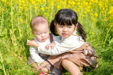 Mart ayında çiçek açan bir tecavüz tarlasında, 6 aylık Japon bir erkek bebek ve 3 yaşındaki ikiz kuyruklu bir kız birlikte oturur, altın çiçeklerle çevrili bahar güneşinin altında atıştırmalıkların tadını çıkarırlar..