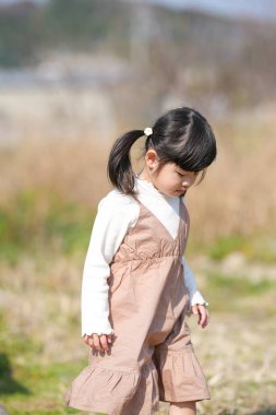 Japonya 'nın kırsal kesiminde, kır çiçekleriyle çevrili çimenli bir arazide oynayan ve Mart ayı sonlarında huzurlu bir öğleden sonra yumuşak bahar güneşinde yıkanan 3 yaşındaki Japon bir kız çocuğu..