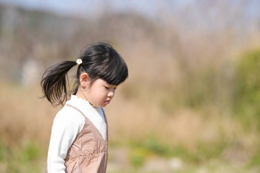 Japonya 'nın kırsal kesiminde, kır çiçekleriyle çevrili çimenli bir arazide oynayan ve Mart ayı sonlarında huzurlu bir öğleden sonra yumuşak bahar güneşinde yıkanan 3 yaşındaki Japon bir kız çocuğu..