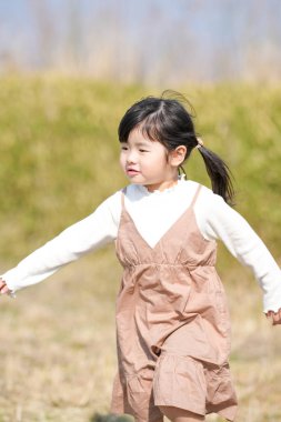 Japonya 'nın kırsal kesiminde, kır çiçekleriyle çevrili çimenli bir arazide oynayan ve Mart ayı sonlarında huzurlu bir öğleden sonra yumuşak bahar güneşinde yıkanan 3 yaşındaki Japon bir kız çocuğu..