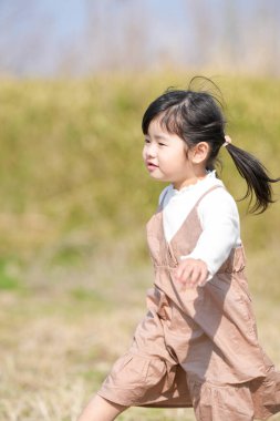 Japonya 'nın kırsal kesiminde, kır çiçekleriyle çevrili çimenli bir arazide oynayan ve Mart ayı sonlarında huzurlu bir öğleden sonra yumuşak bahar güneşinde yıkanan 3 yaşındaki Japon bir kız çocuğu..