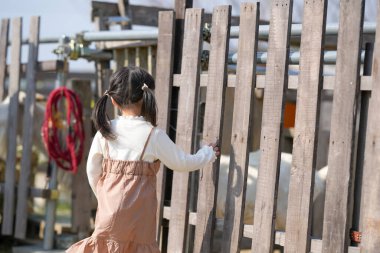 İkiz kuyruklu neşeli bir Japon kızı, Mart ayında güneşli bir bahar öğleden sonrasını sakin bir kırsal alanda yumuşak, sıcak güneş ışığıyla yıkanmış bir keçiyi yeşil otla besleyerek geçiriyor..