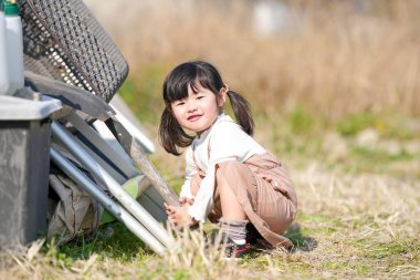 İkiz kuyruklu 3 yaşındaki Japon bir kız, Japonya 'nın kırsal kesimindeki çimenlik bir alanda, dağınık malzemelerle çevrili bir depoda oynuyor ve Mart ayı sonlarında yumuşak bahar güneşinde banyo yapıyor..