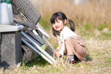 İkiz kuyruklu 3 yaşındaki Japon bir kız, Japonya 'nın kırsal kesimindeki çimenlik bir alanda, dağınık malzemelerle çevrili bir depoda oynuyor ve Mart ayı sonlarında yumuşak bahar güneşinde banyo yapıyor..