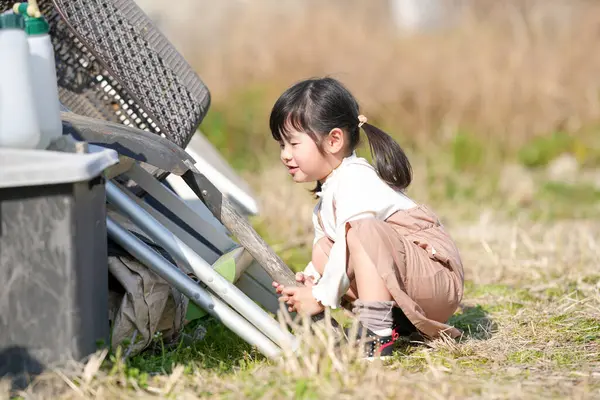 İkiz kuyruklu 3 yaşındaki Japon bir kız, Japonya 'nın kırsal kesimindeki çimenlik bir alanda, dağınık malzemelerle çevrili bir depoda oynuyor ve Mart ayı sonlarında yumuşak bahar güneşinde banyo yapıyor..